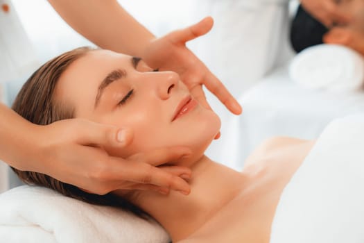 Caucasian couple enjoying relaxing anti-stress head massage and pampering facial beauty skin recreation leisure in dayspa modern light ambient at luxury resort or hotel spa salon. Quiescent