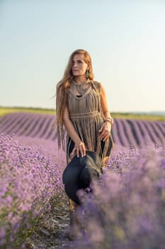 A woman is standing in a field of purple flowers, wearing a black dress and a black hat