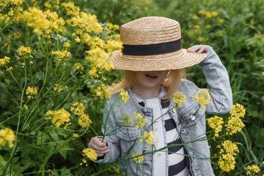 Blonde girl in a field with yellow flowers. A girl in a straw hat is picking flowers in a field. A field with rapeseed