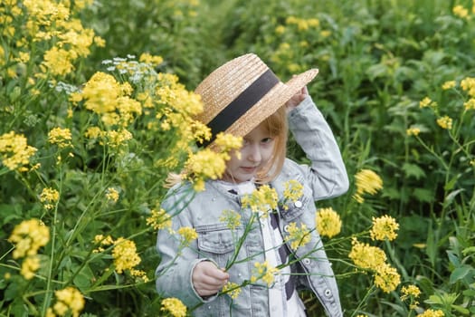 Blonde girl in a field with yellow flowers. A girl in a straw hat is picking flowers in a field. A field with rapeseed