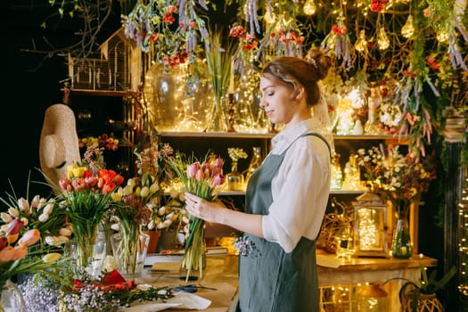 A woman in her florist shop collects bouquets of flowers. The concept of a small business. Bouquets of tulips for the holiday on March 8