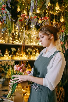 A woman in her florist shop collects bouquets of flowers. The concept of a small business. Bouquets of tulips for the holiday on March 8