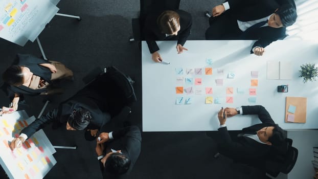 Top down aerial view of business group sharing and brainstorming idea by using sticky notes at meeting room. Investor writing marketing strategy on board while receive note from manager. Directorate.