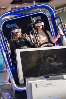 Moscow, Russia, March 14, 2024. Two woman is sitting in an electric blue virtual reality chair, wearing a headset. The machine combines engineering and fun in a display device