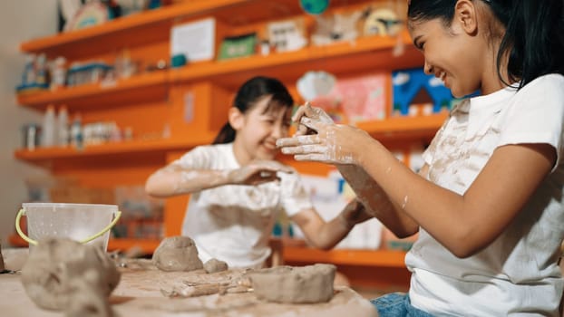 Happy multicultural girl and friend put the clay on the each other muddy shirt at art lesson. Diverse highschool student playing with clay at pottery workshop. Creative activity concept. Edification.