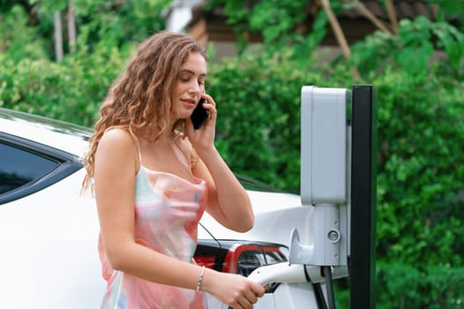 Modern eco-friendly woman recharging electric vehicle from home EV charging station. Innovative EV technology utilization for tracking energy usage to optimize battery charging at home. Synchronos