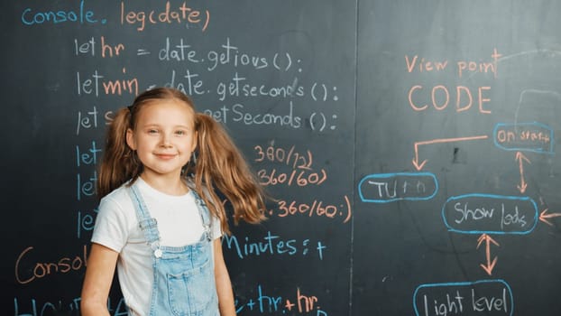 Happy caucasian girl looking at camera while standing at board with engineering prompt or coding, programing system written in STEM technology classroom. Pretty student smile at camera. Erudition.