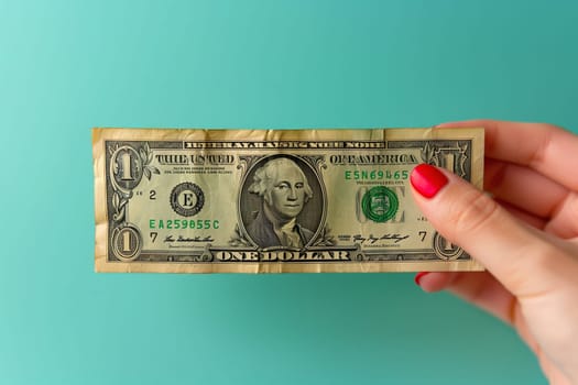 A green rectangle of currency, a collectable banknote, is being held by a womans hand with red nails. Her fingers and thumbs clutch the cash, ready for travel