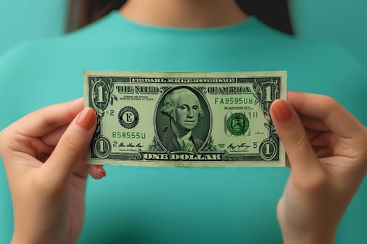 The womans hand is holding a banknote with her fingers and thumb. She is gesturing towards the currency in her hand, showcasing the font and details of the dollar bill