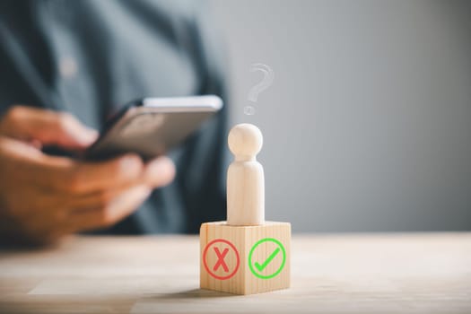 Using smartphones businessman checks right or wrong symbols on wooden block for yes or no decision-making. Communication of choice and achievement. Think With Yes Or No Choice.