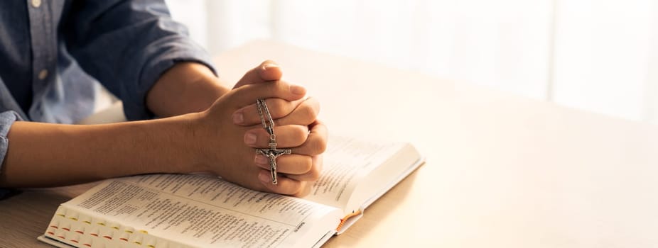 Asian male folded hand prayed on holy bible book while holding up a pendant crucifix. Spiritual, religion, faith, worship, christian and blessing of god concept. Blurring background. Burgeoning.