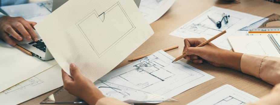 Skilled architect drafts blueprint on paper while male engineer works on laptop in architectural office. Professional engineer and architect collaborate on architectural project. Closeup. Delineation.