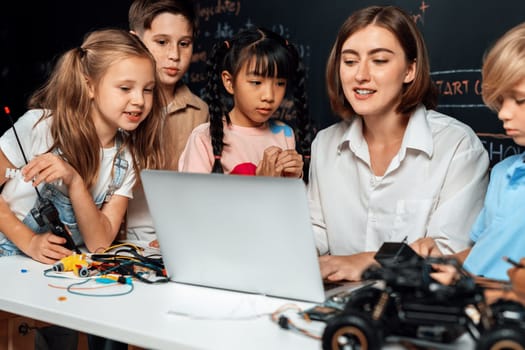 Teacher coding to demonstrate children how to code robots in the STEM class. Children fun to watch how teacher coding with confident only boy in blue shirt taking note with serious look. Erudition.