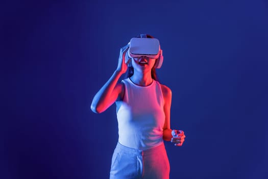 Smart female stand in cyberpunk neon light wearing VR headset connecting metaverse, futuristic cyberspace community technology. Elegant woman excited seeing generated virtual scenery. Hallucination.