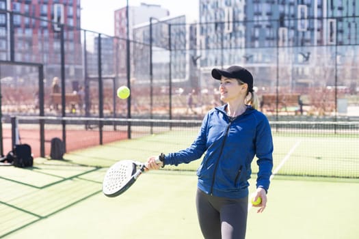 A girl in sportswear is training on a paddle tennis court. The girl is hitting the ball against the glass to make a rebound. Concept of women playing paddle. High quality photo