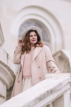 woman in elegant coat and hat against an intricate architectural backdrop, harmoniously blending modern fashion with historical allure. The soft daylight adds to its timeless appeal