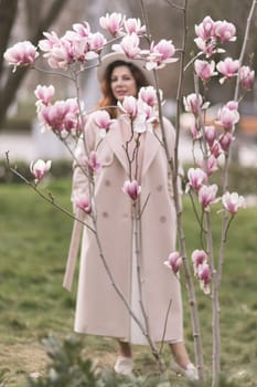 Woman magnolia flowers, surrounded by blossoming trees, hair down, white hat, wearing a light coat. Captured during spring, showcasing natural beauty and seasonal change