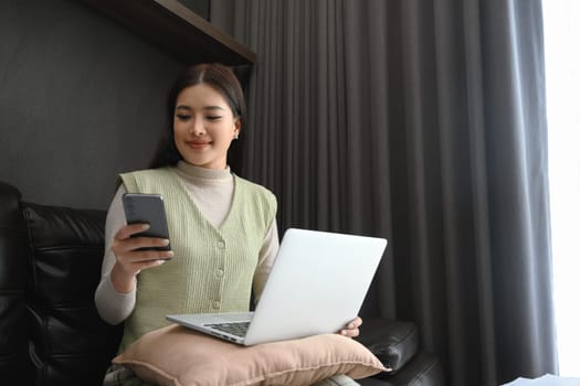 Beautiful female entrepreneur using mobile phone and laptop at home.