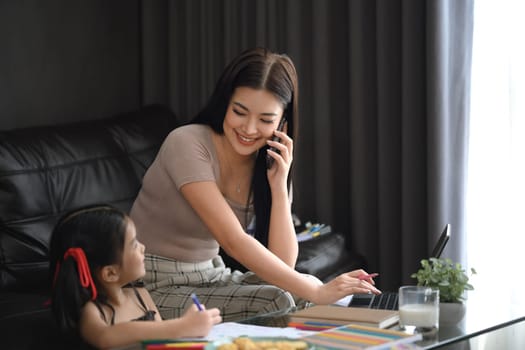 Happy single mom working remotely at home and looking at her daughter painting.