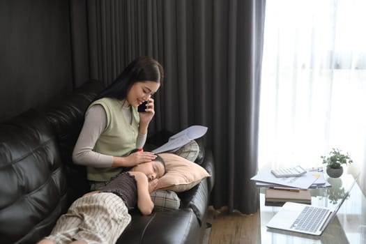 Happy young mother freelancer working at home sitting on sofa with her little daughter.