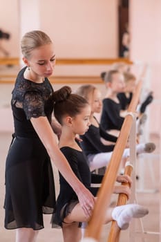 Caucasian woman teaches little girls ballet at the barre. Vertical photo