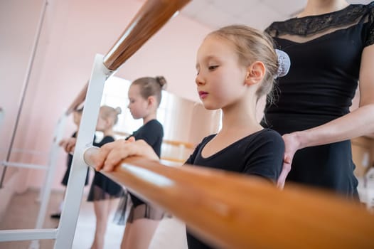 Caucasian woman teaches little girls ballet at the barre