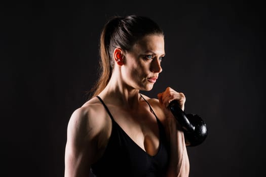 Tough fitness female model with kettle bell on a grey dark yellow red background.