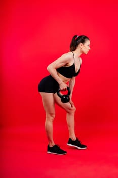 Tough fitness female model with kettle bell on a grey dark yellow red background.