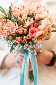 woman holding bouquet of pink flowers with white accents. The bouquet is tied with a blue ribbon