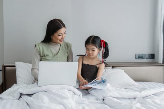 Work from home, freelance and lifestyle concept. Portrait of creative asian female sitting on bed with laptop and her take care of her kid while working.