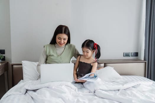 Work from home, freelance and lifestyle concept. Portrait of creative asian female sitting on bed with laptop and her take care of her kid while working.