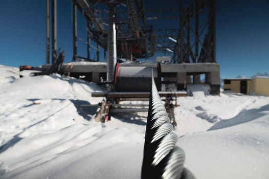 A cable car station under construction high in the mountains in winter. Focus on a close-up of a thick cable car cable covered with snow.