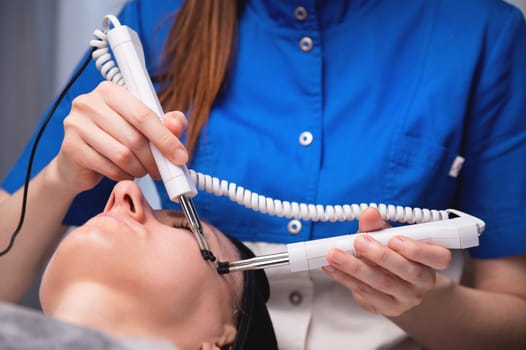 A middle-aged woman undergoes electrotherapeutic facial rejuvenation procedures in a cosmetologist's office