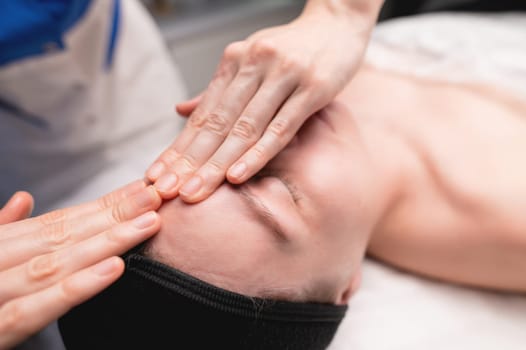 A Caucasian woman gets a facial massage in a cosmetology salon. Woman receiving massage for rejuvenation.