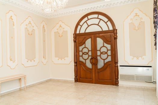 A large wooden door with a glass window in the middle. The room is empty and has a very elegant and sophisticated look