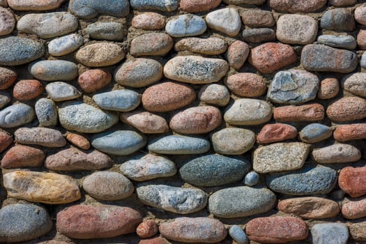 wall made of many colorful round stones under direct sun light, full-frame background and texture.