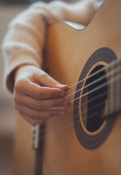 A beautiful little caucasian girl holds a guitar and plucks the strings with her fingers, close-up side view. Music education concept.