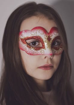 Portrait of a beautiful caucasian brunette girl with long flowing hair in a carnival mask on her face looking at the camera,side view close-up.Carnivals time concept.