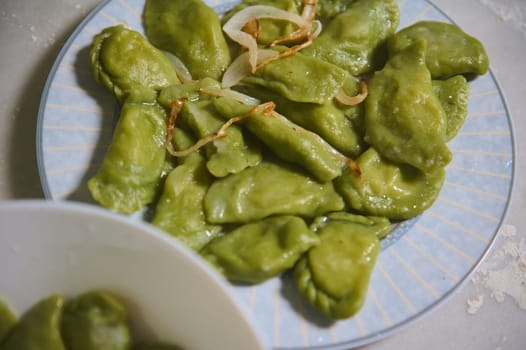 Top view of Ukrainian dumpling Varennyky of green color dough with spinach, stuffed with mashed potato and roasted with onion. Food background. Food blogging