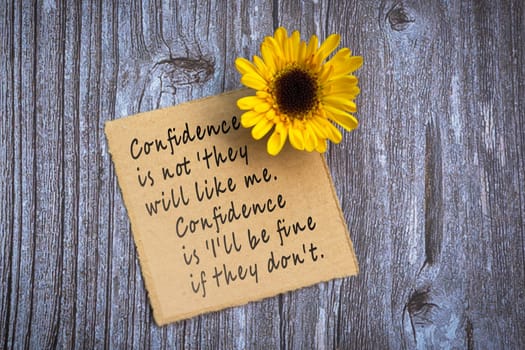 Motivational on brown note with gerbera yellow flower on wooden surface - Confidence is not they will like me, confidence is i will be fine if they do not.