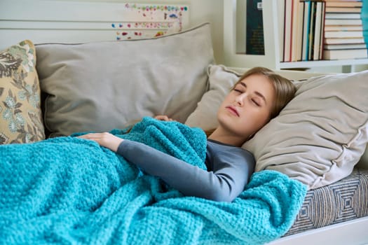 Sleeping relaxed resting young teenage female, with her eyes closed, lying on pillow under blanket at home on couch. Health, rest calm peace, beauty, lifestyle, youth concept