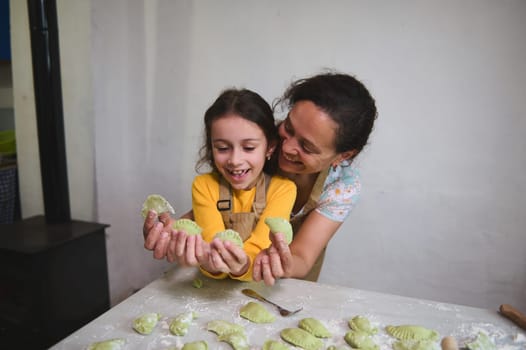 Mother and daughter have fun while cooking dumplings, standing together at floured kitchen table