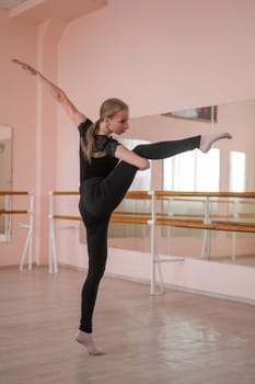 Caucasian woman lifts her leg into a split in a dance hall with a ballet barre. Vertical photo