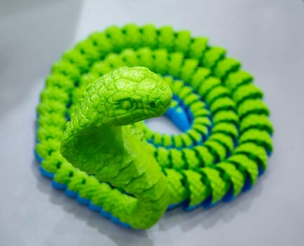 Green snake toy model printed on a 3D printer from melted plastic. Snake-shaped object created by 3D printer. Detailed green prototype printed on 3D printer close-up. New modern additive technologies