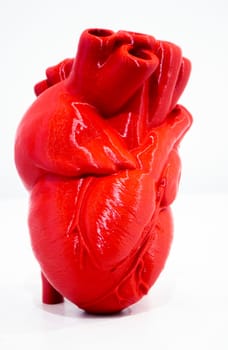 A prototype of a human heart 3D printed from molten red plastic. Model of a human heart printed on a 3D printer isolated on a white background. New modern additive 3D printing medical technologies