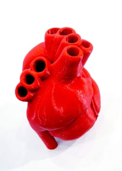 A prototype of a human heart 3D printed from molten red plastic. Model of a human heart printed on a 3D printer isolated on a white background. New modern additive 3D printing medical technologies