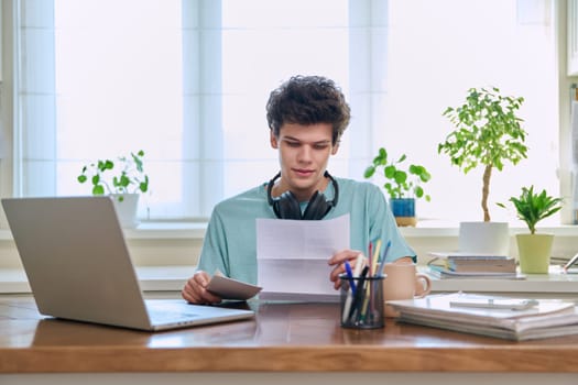 Serious young guy, student of 19-20 years old, reading letter, paper document.