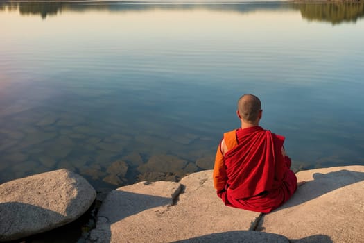 The image shows a person sitting on a rock in the middle of a body of water, with mountains in the background.