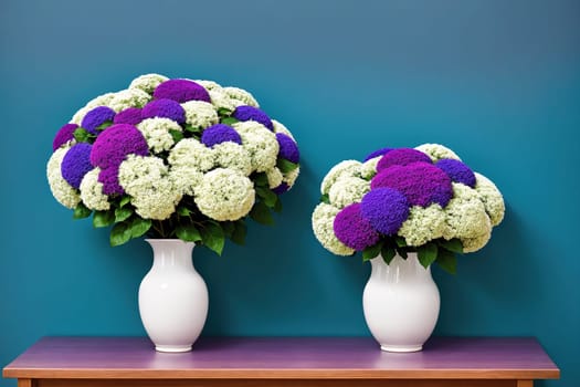 Two vases filled with white flowers sit on a table in front of a blue wall.