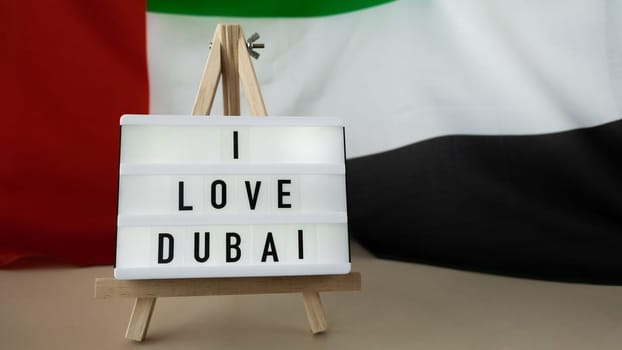 Message text I LOVE DUBAI on background of waving UAE flag made from silk. United Arab Emirates flag with concept of tourism and traveling. Inviting greeting card, advertisement. Dubai welcoming card